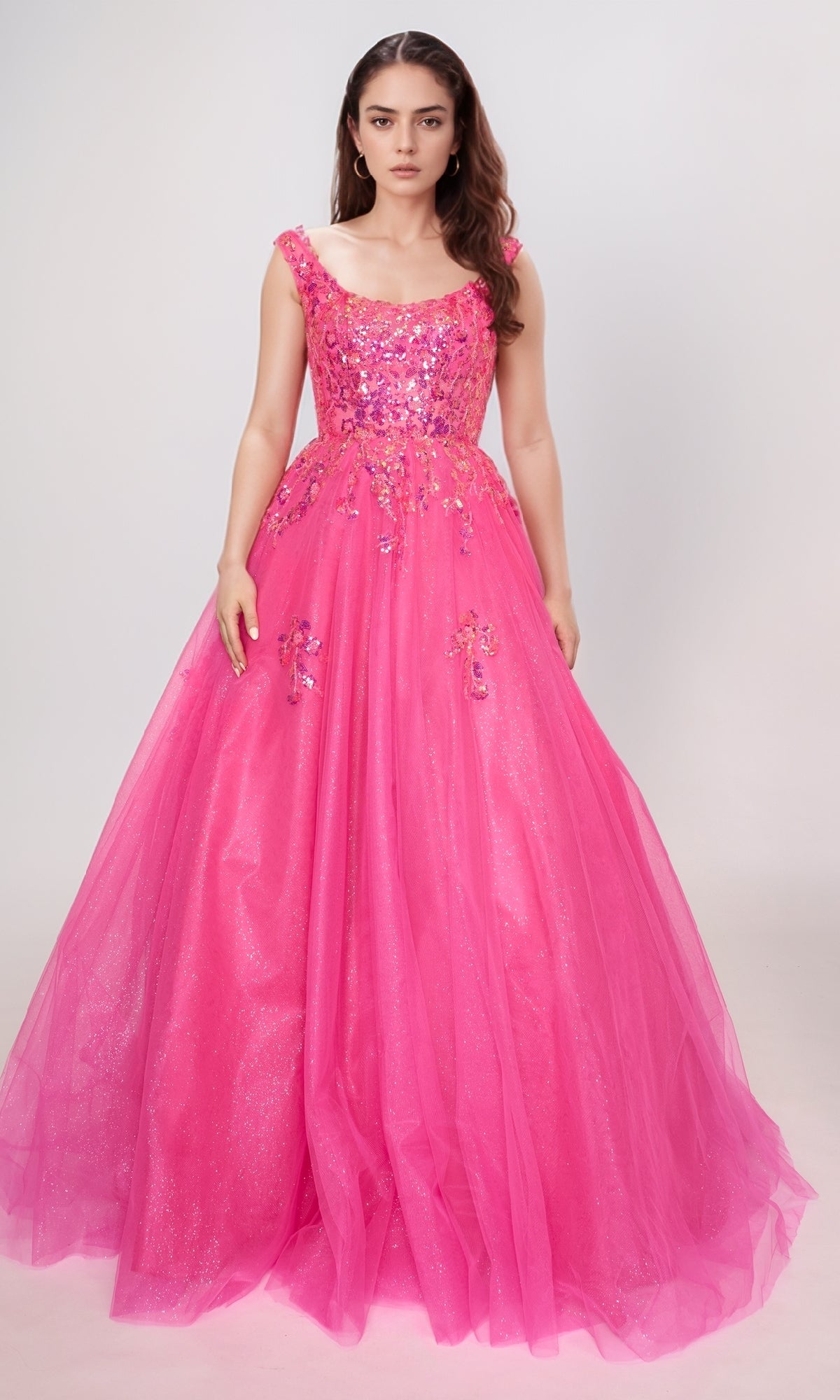 A woman poses against a plain background in the Long Prom Dress: Nina Canacci 3266, a bright pink gown with glitter tulle, sequins, and floral embellishments.